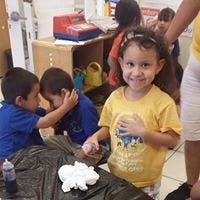 Child in yellow shirt smiling at camera, other children in background