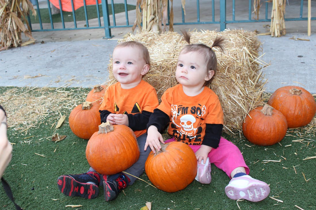 Two children in orange shirts sitting with pumpkins