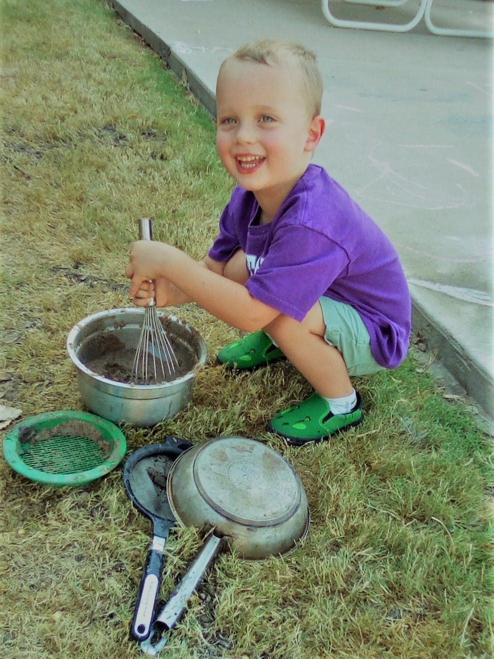 Child mixing dirt in a bowl with a whisk