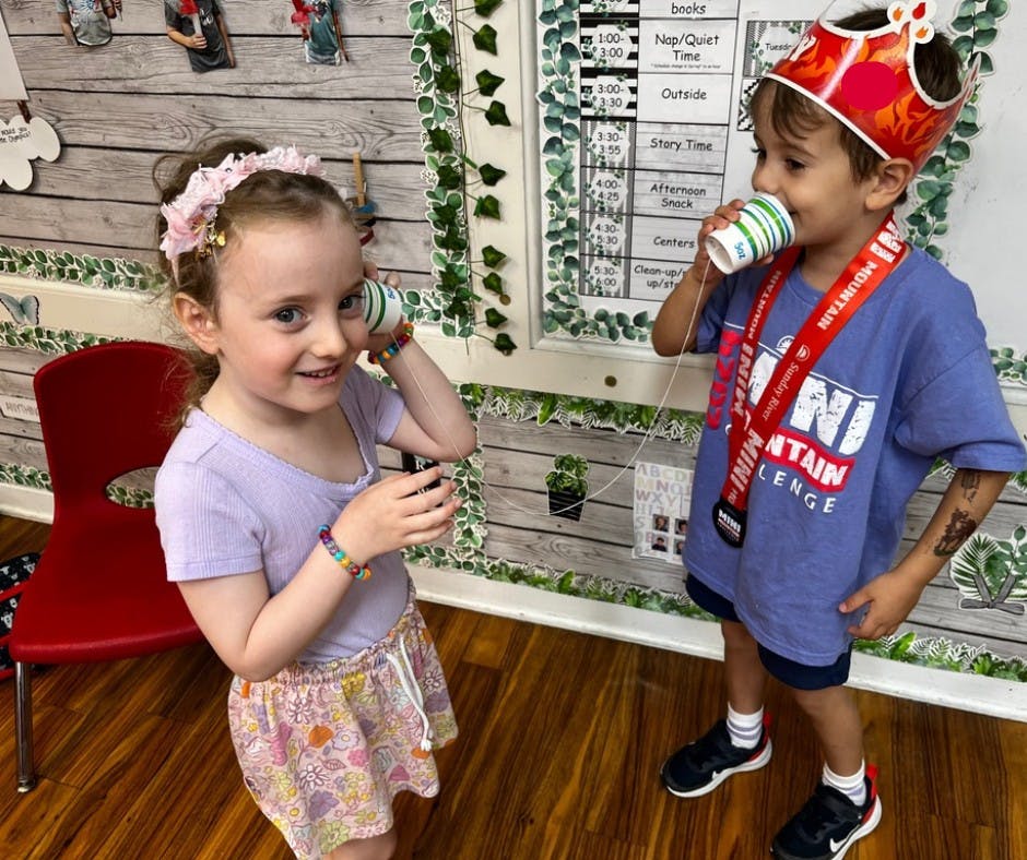 Two children playing with paper cups as string telephones