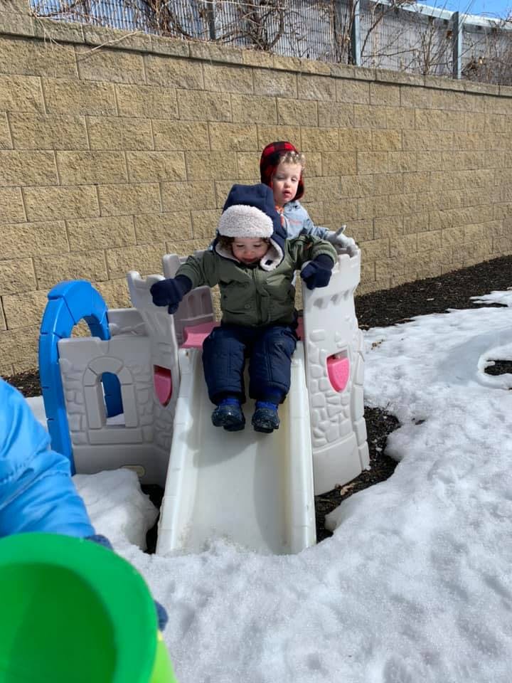 Child in winter clothes on a small slide in the snow