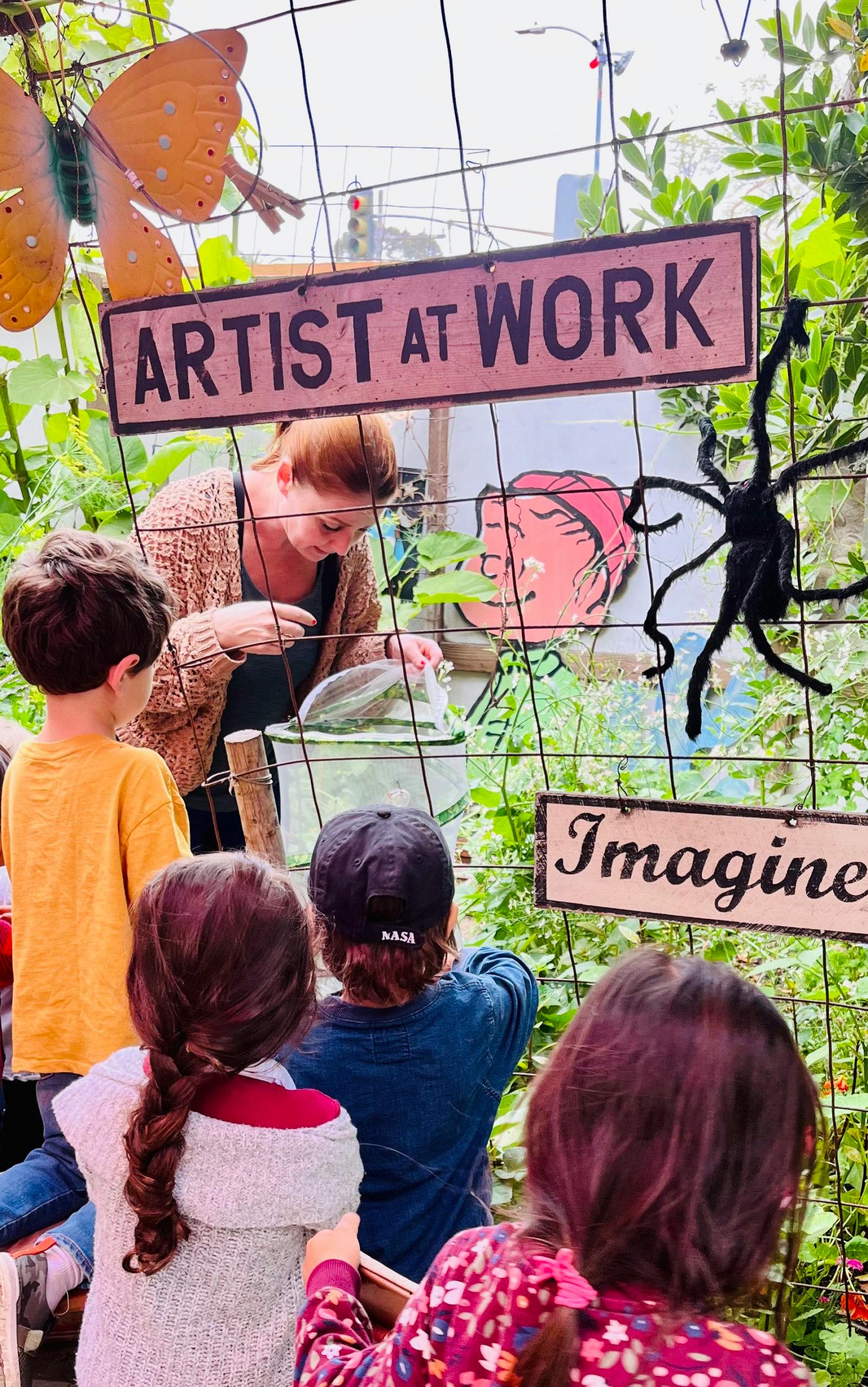 Person showing a butterfly enclosure to several children through a fence