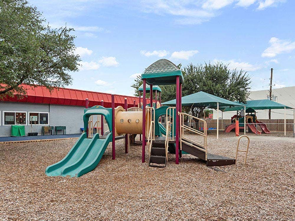 A playground with slides, climbing structures, and shade canopies over wood chips
