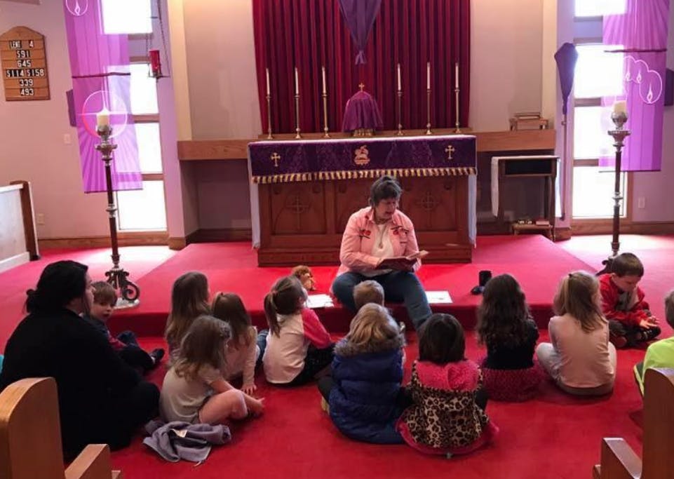 Person reading to children sitting on a red carpet