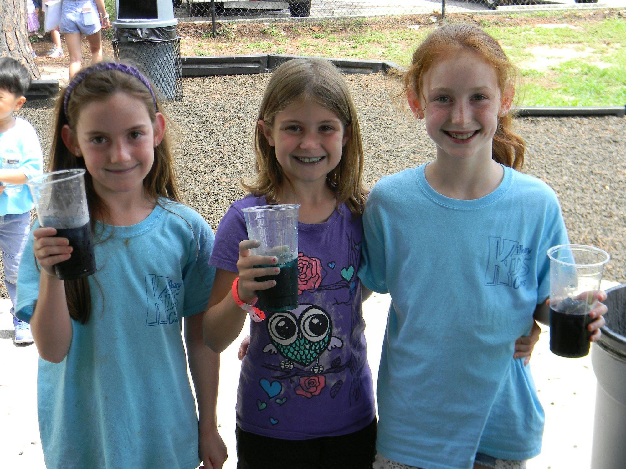 Three children holding cups with dark liquids