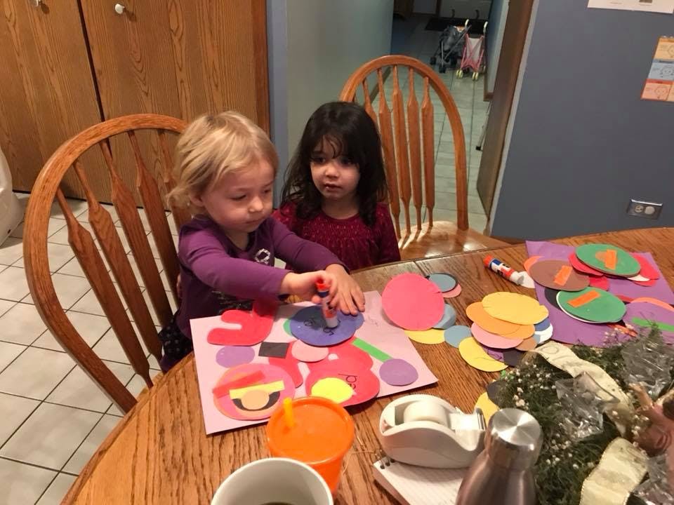 Two children sitting at a table doing crafts with colorful paper cutouts