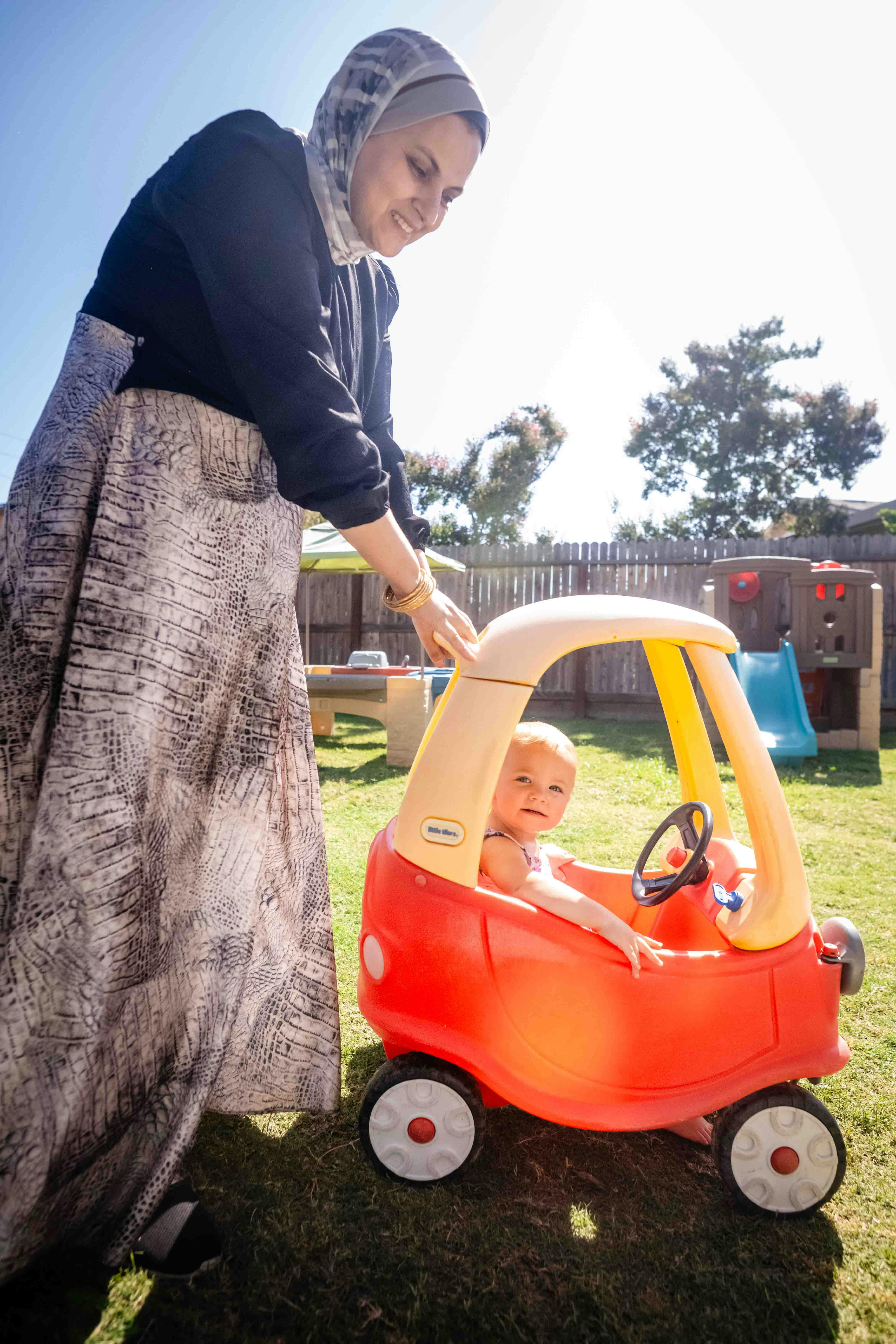 Person pushing a child in a toy car outdoors