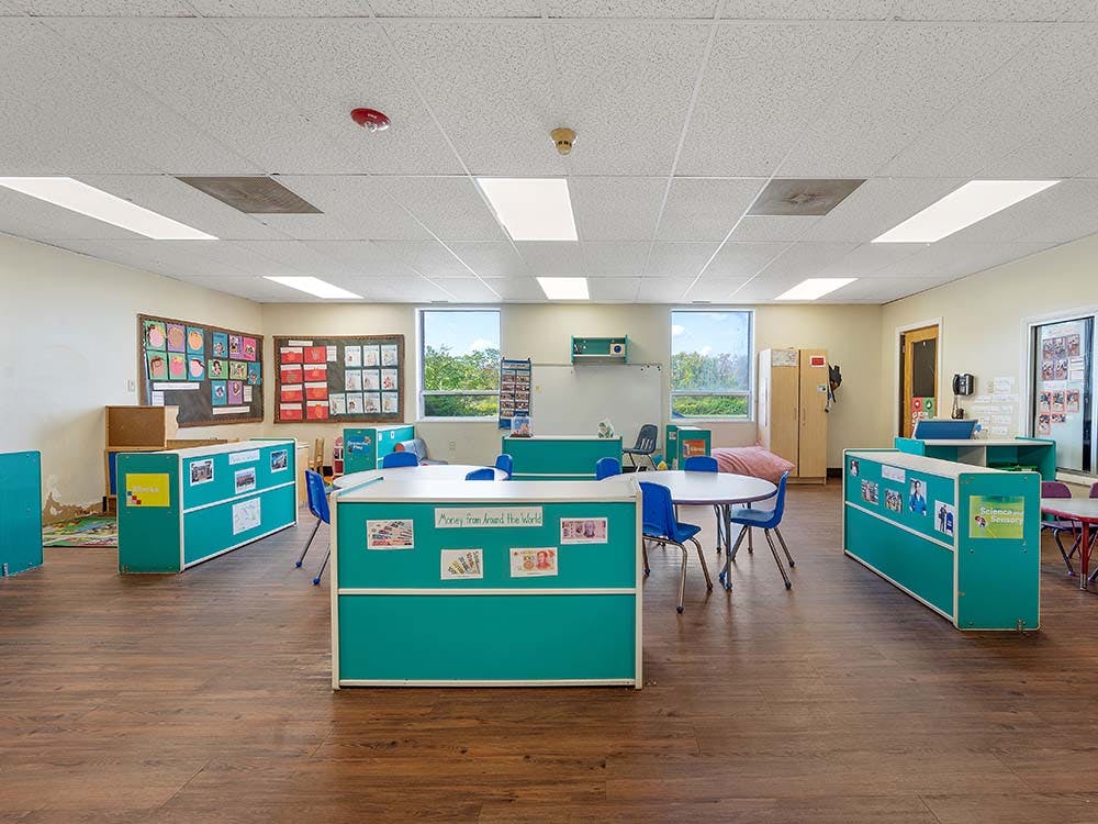 Empty classroom with teal dividers, white tables, and blue chairs