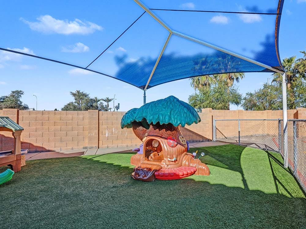 Child's treehouse play structure on artificial grass under a blue shade canopy