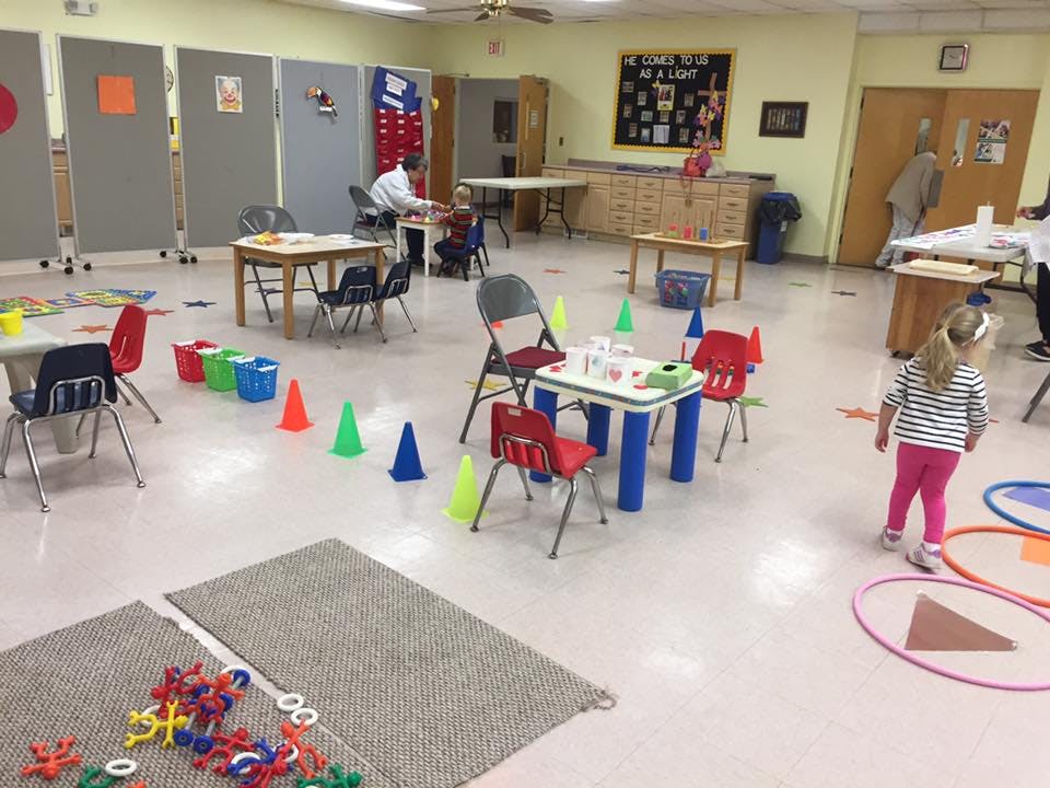 Child walking in a classroom with tables, chairs, and cones