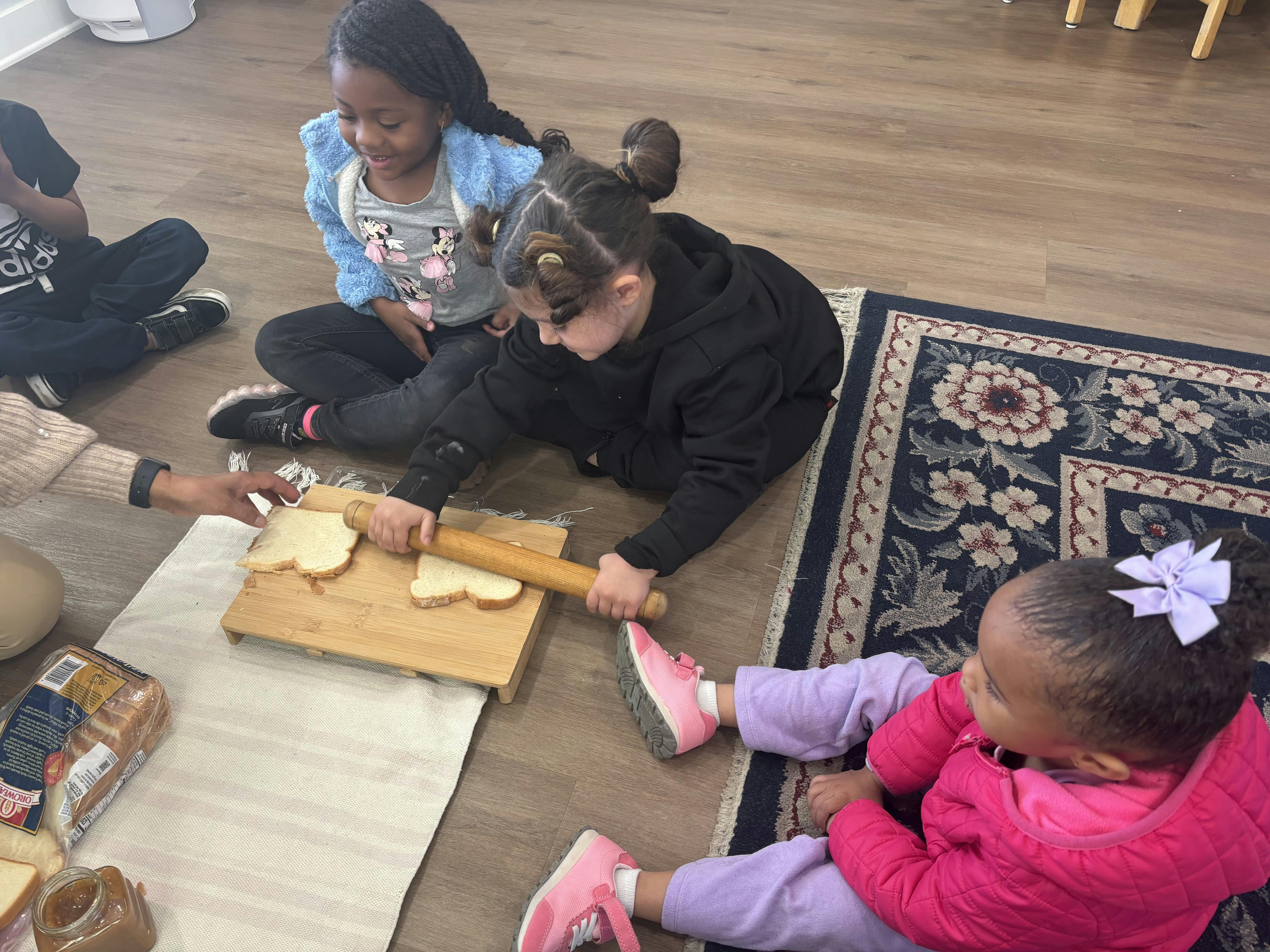 Child rolling bread with a rolling pin on a wooden board while other children watch