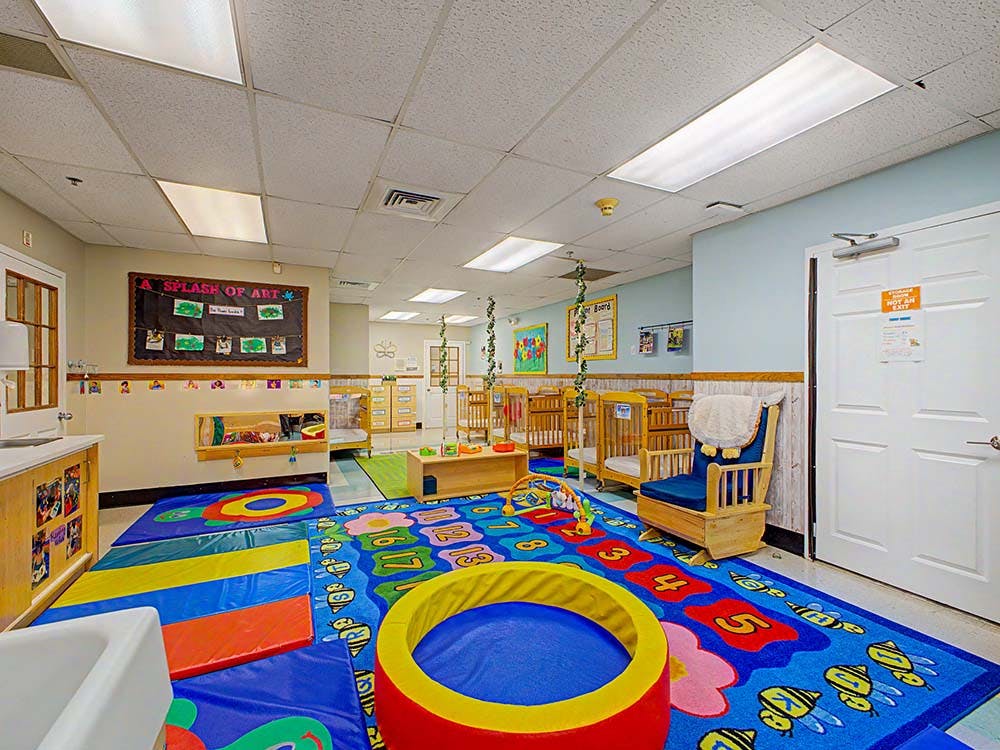 a brightly lit nursery classroom with cribs and colorful play mats