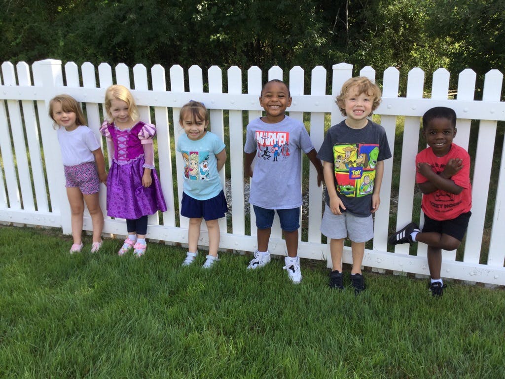 Six children standing in front of a white picket fence