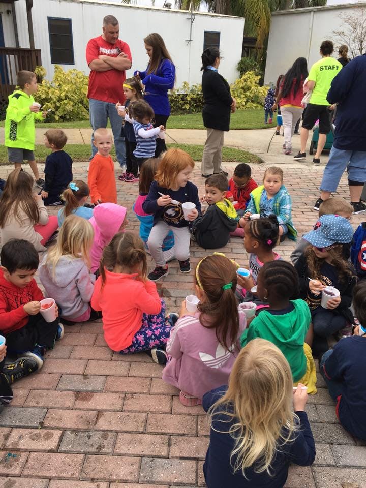 Children sitting on the ground with adults standing in the background