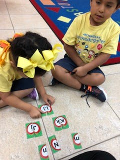Two children playing with alphabet letter cards on the floor