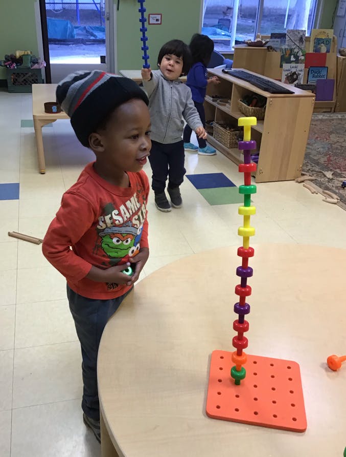 Child in a beanie looking at a colorful stacking toy on a table
