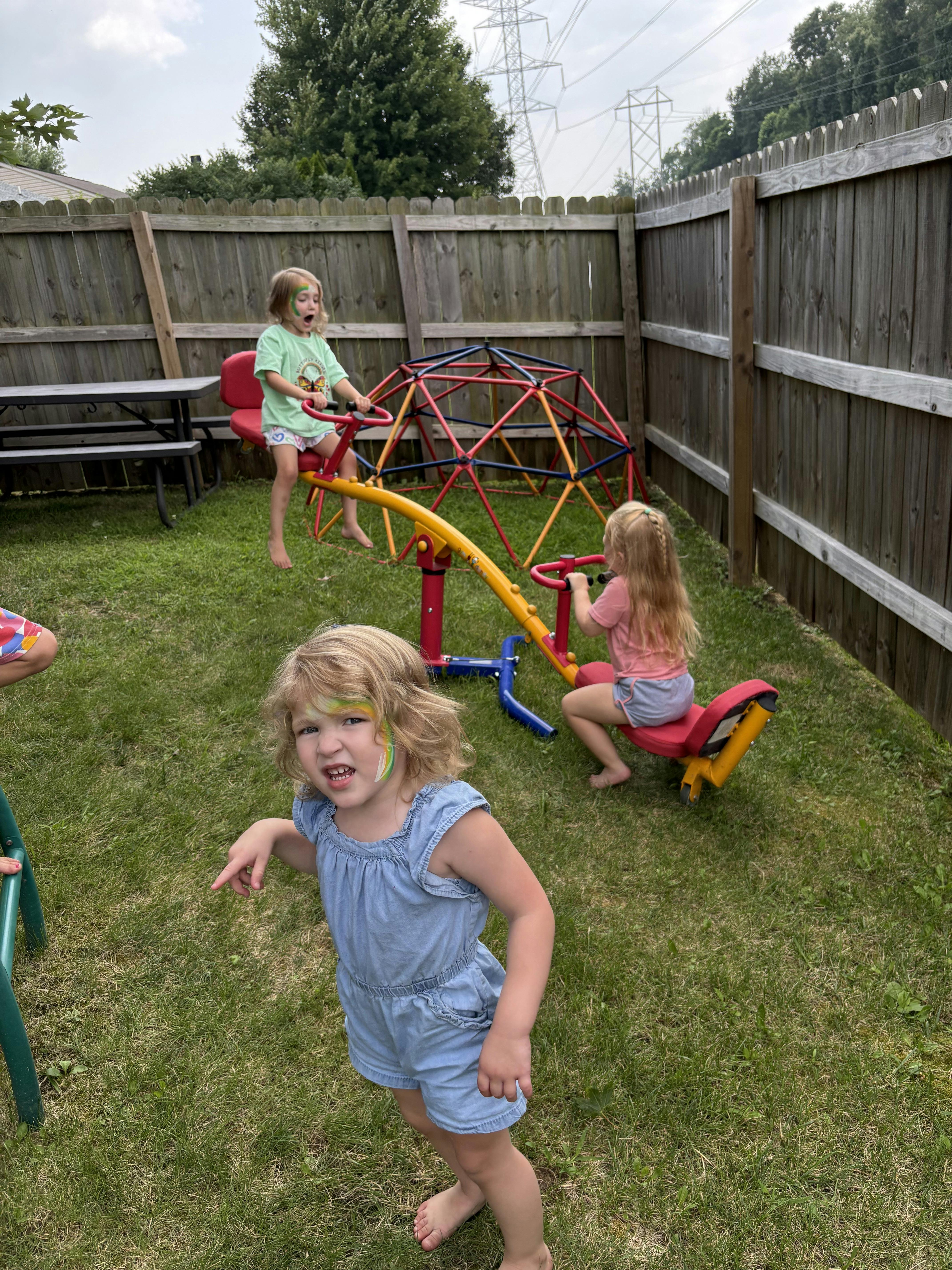 Children playing on a seesaw and a jungle gym in a grassy backyard