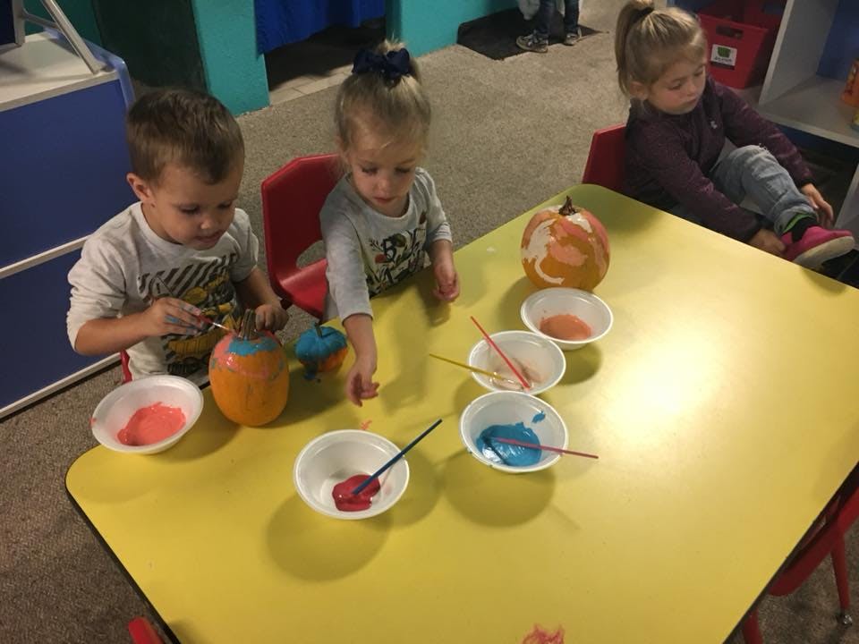 Children painting pumpkins at a table