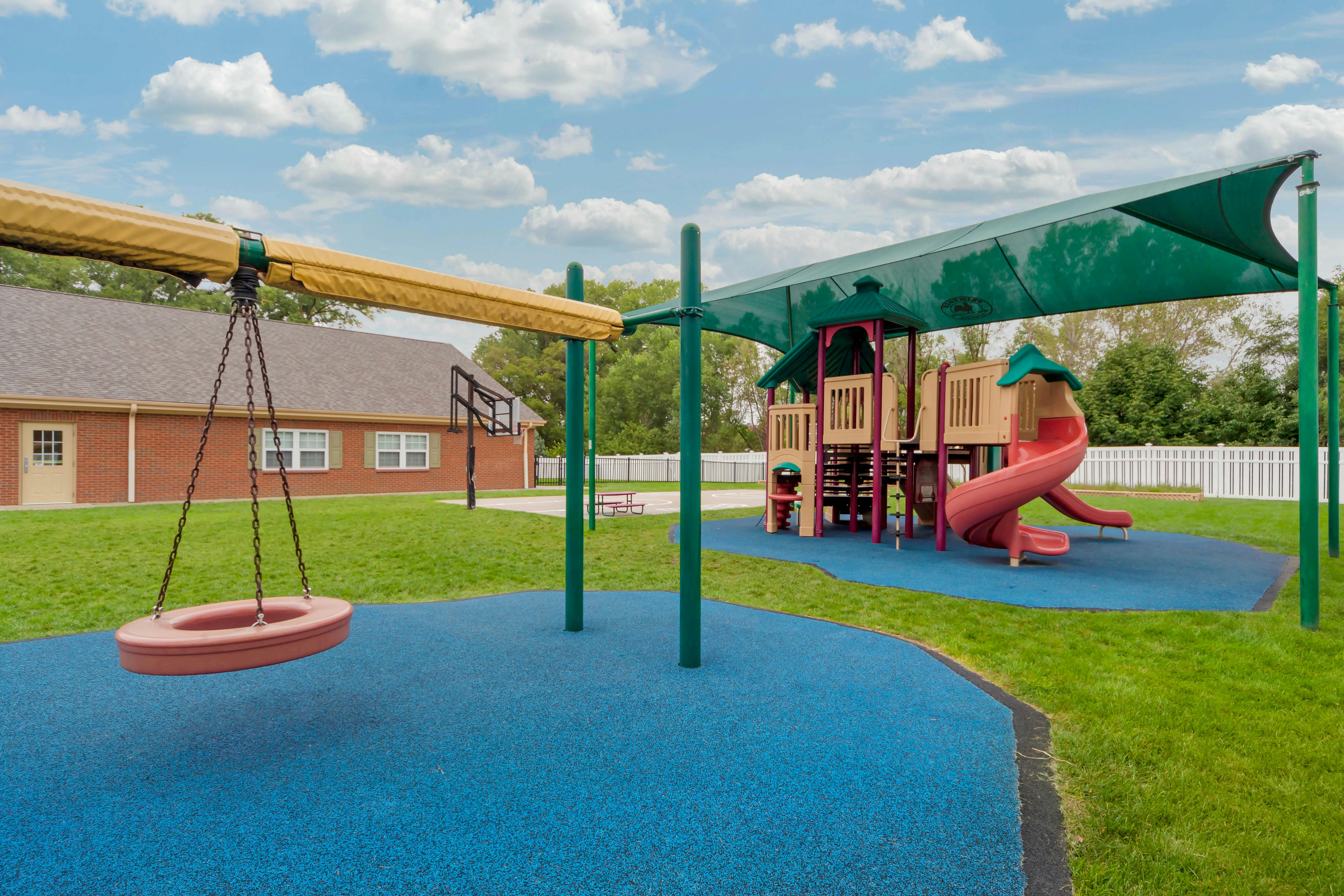 Playground with swings, slides, and climbing structures on blue ground with grass around it