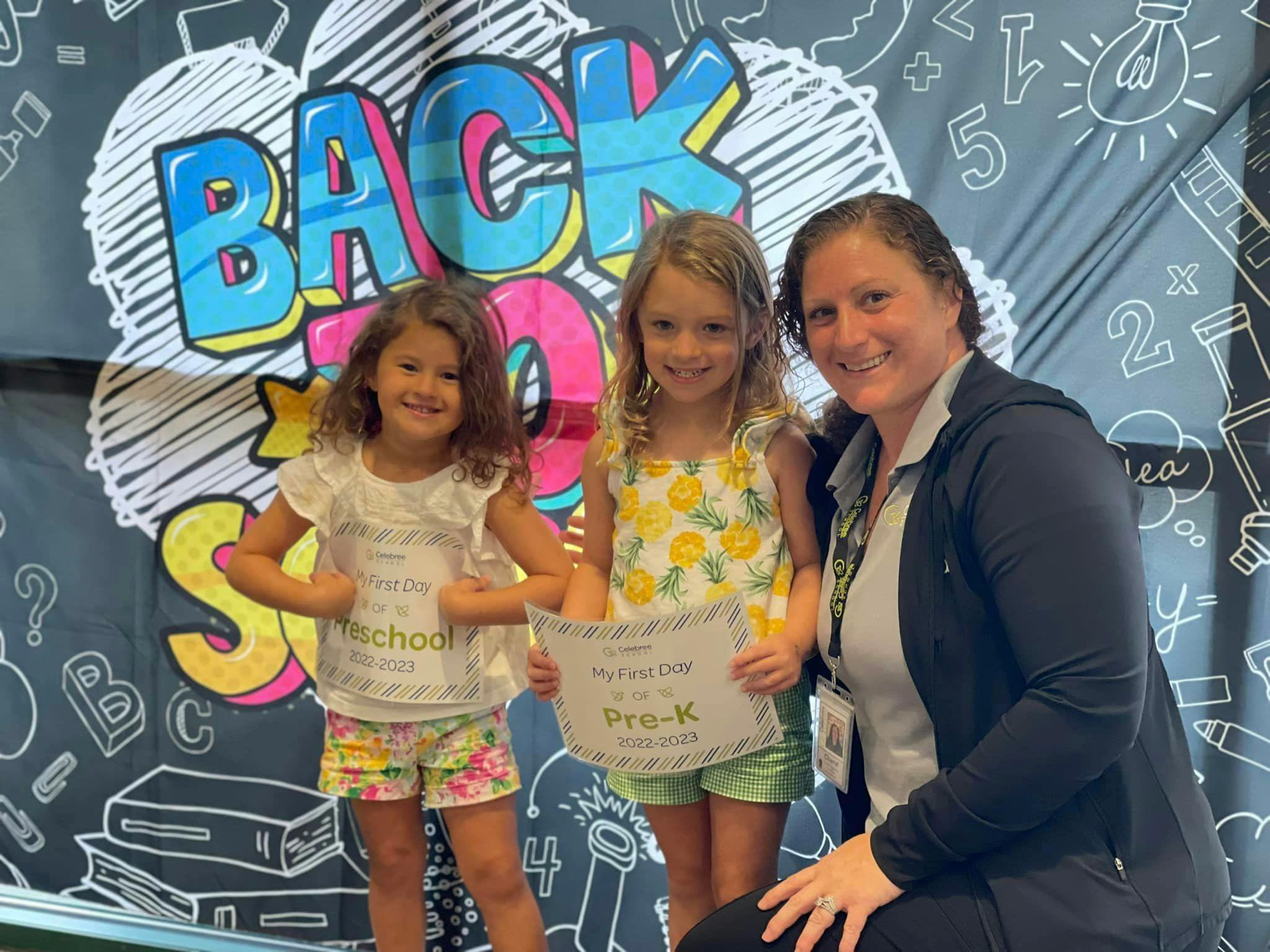 Two children and an adult posing with a certificate in front of a "Back to School" sign