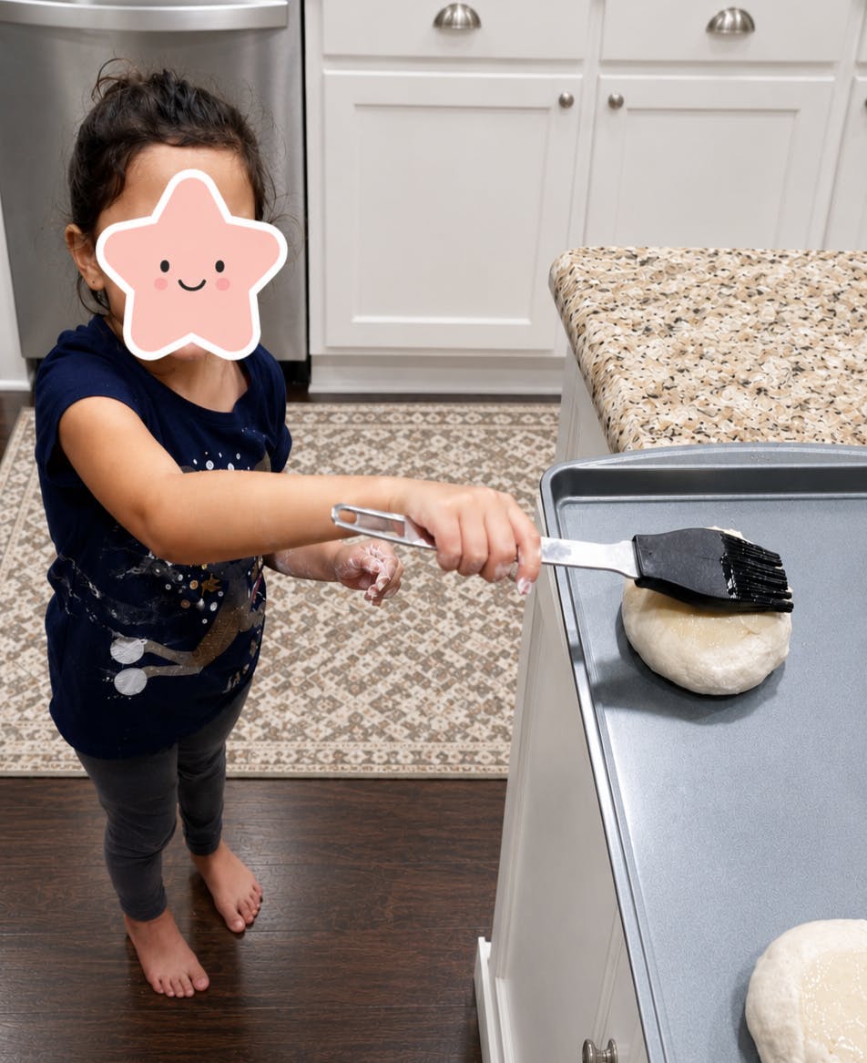 Child brushing dough on a baking sheet in a kitchen