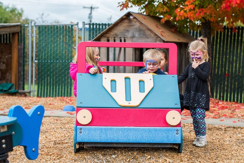 Three children playing in a toy car on a playground