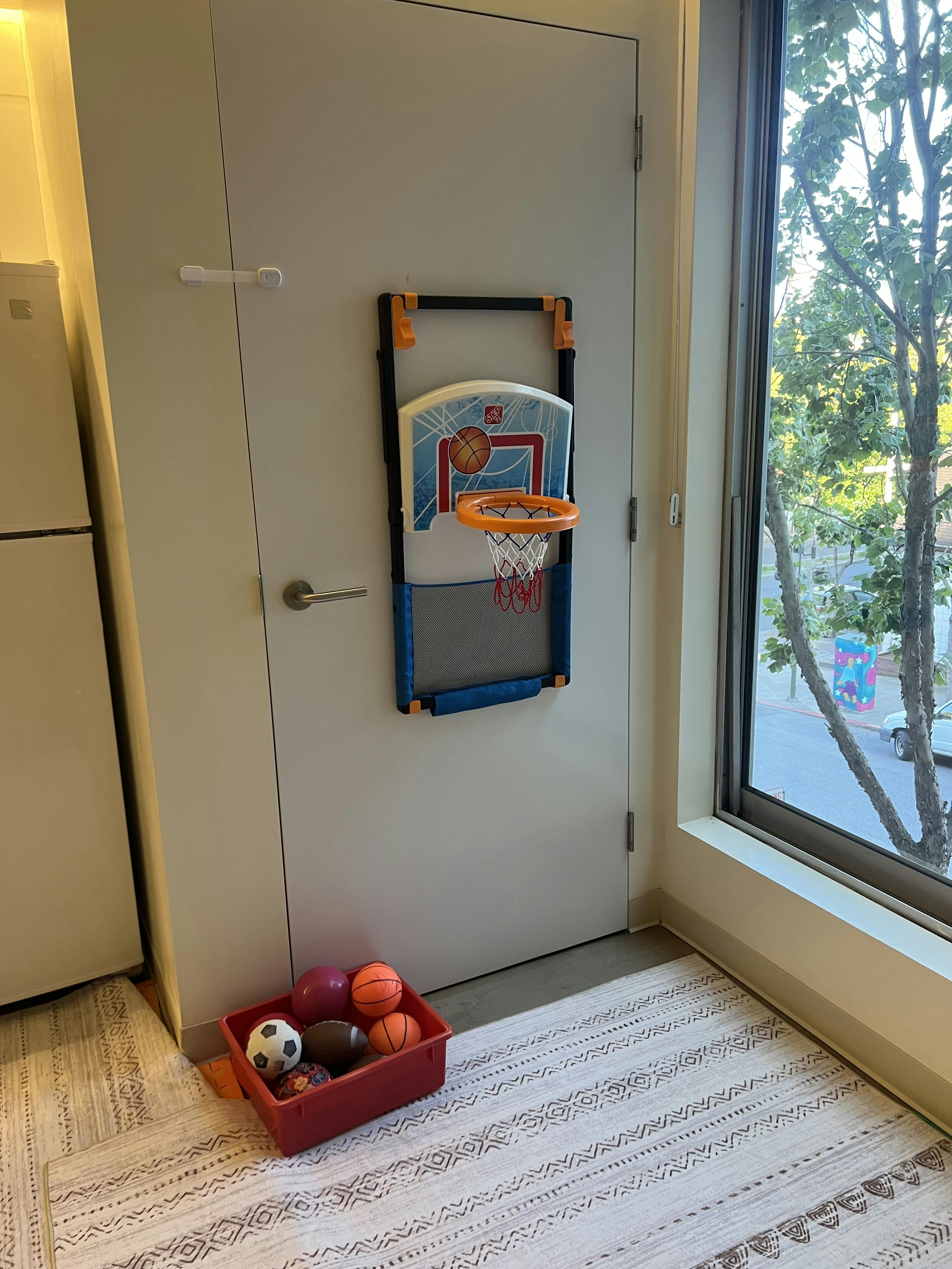 Basketball hoop attached to a door with a bin of balls on the floor