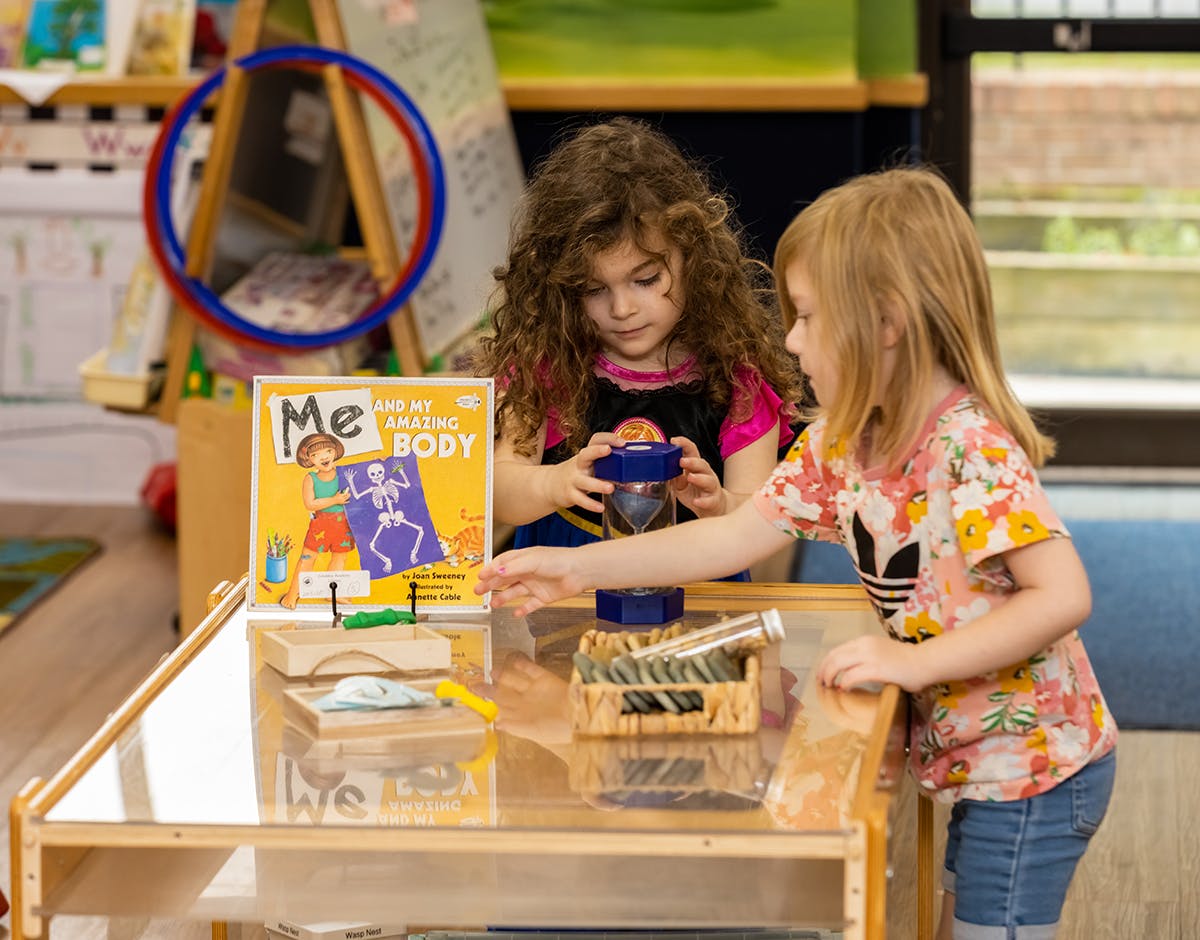 Two children playing with items on a table, one reaching for an object