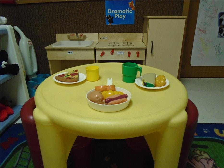 Toy food on a yellow play table in a classroom with a sign that reads Dramatic Play