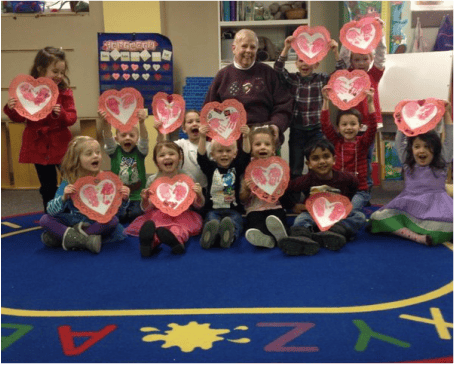 Adult and children holding up heart-shaped crafts in a classroom
