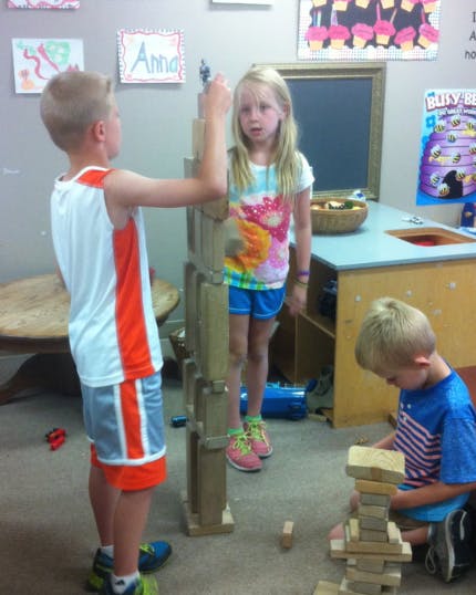 Three children playing with wooden blocks in a classroom