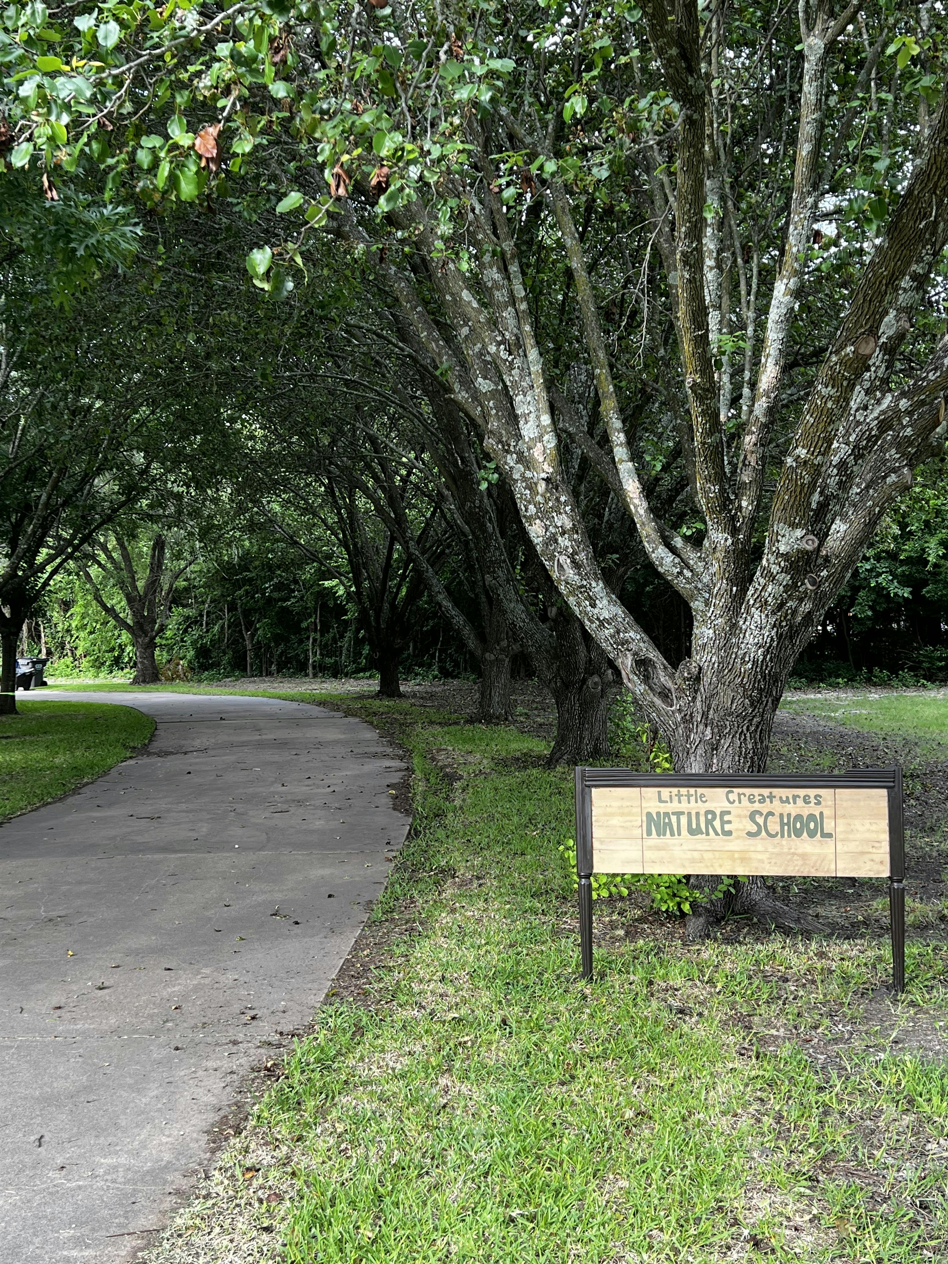 Sign for Little Creatures Nature School next to a winding paved path and trees