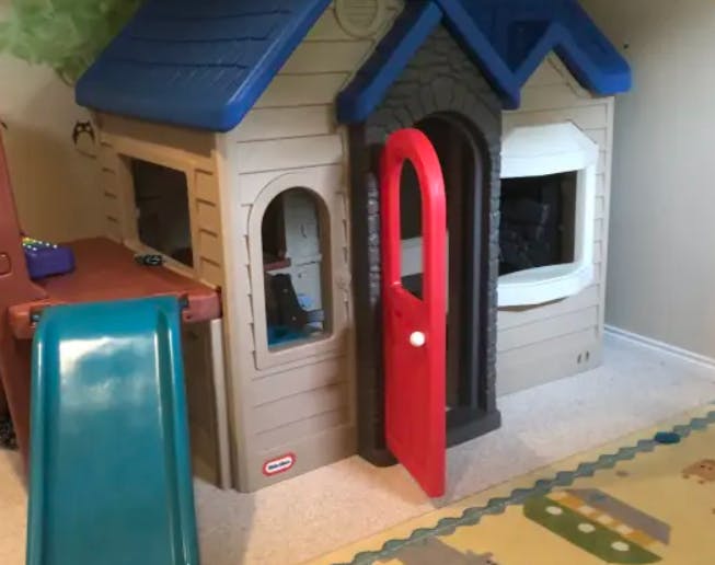 Child's playhouse with a red door and a blue slide