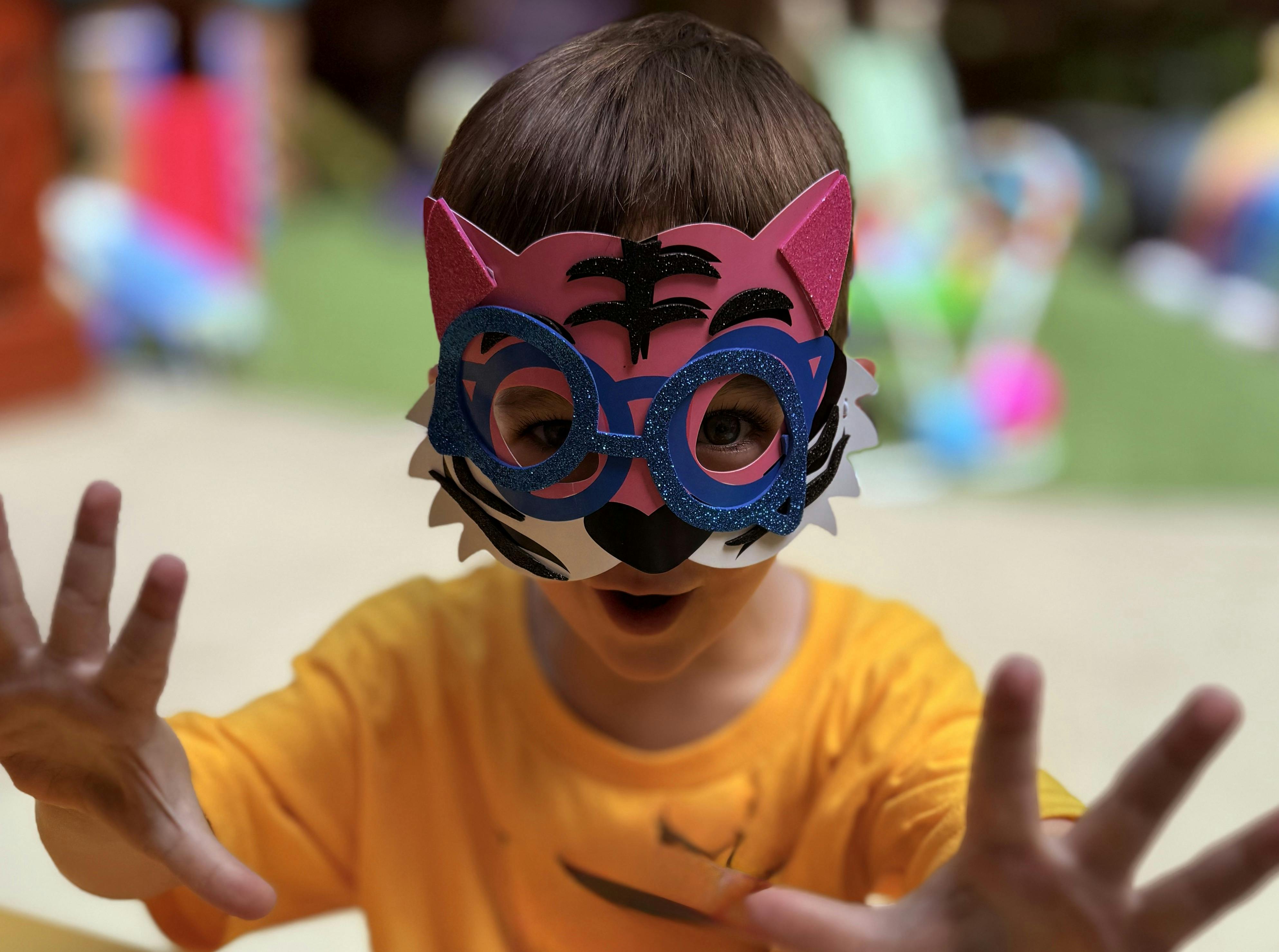 Child wearing a pink and blue tiger mask with hands raised