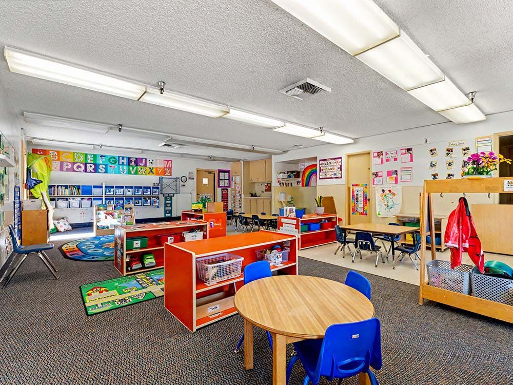 Colorful classroom with small tables and chairs, shelves, and alphabet decoration