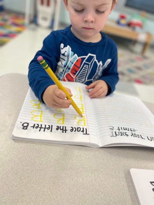 Child tracing letters in a notebook with a pencil
