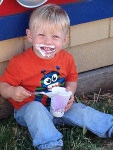 Child with messy face holding a cup and spoon
