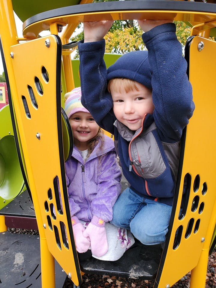 Two children playing inside a yellow structure on a playground