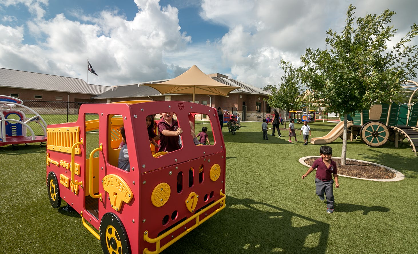 Children playing on a red toy truck and other playground equipment