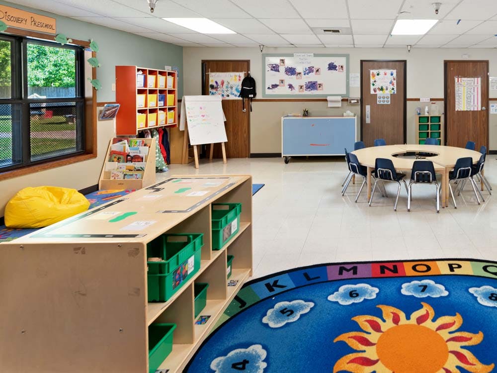 An empty preschool classroom with tables, chairs, and shelves