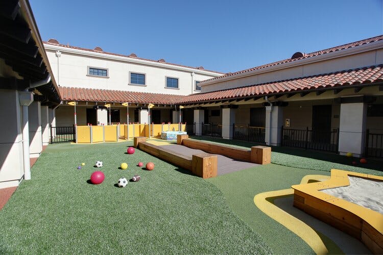 Outdoor courtyard with artificial grass, play structures, and balls