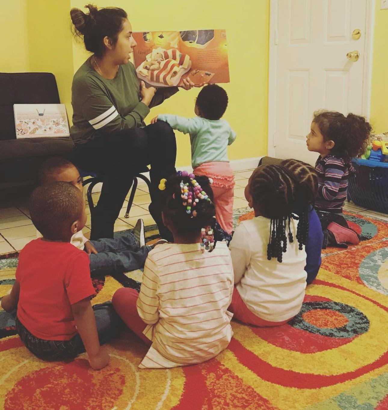 person reading a book to several children sitting on a colorful rug