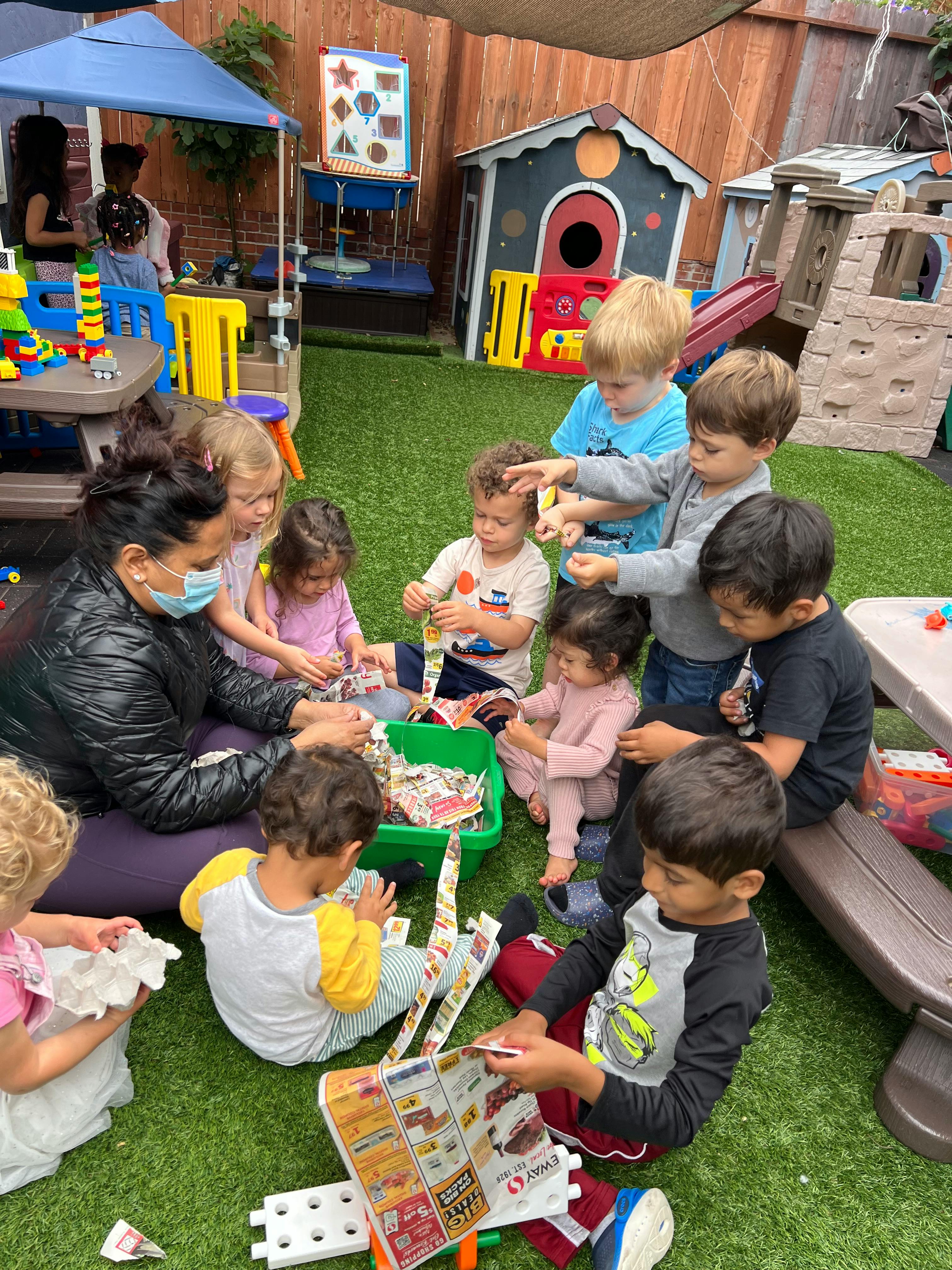 Adult and children sitting on grass, engaged in an activity with paper and paper
