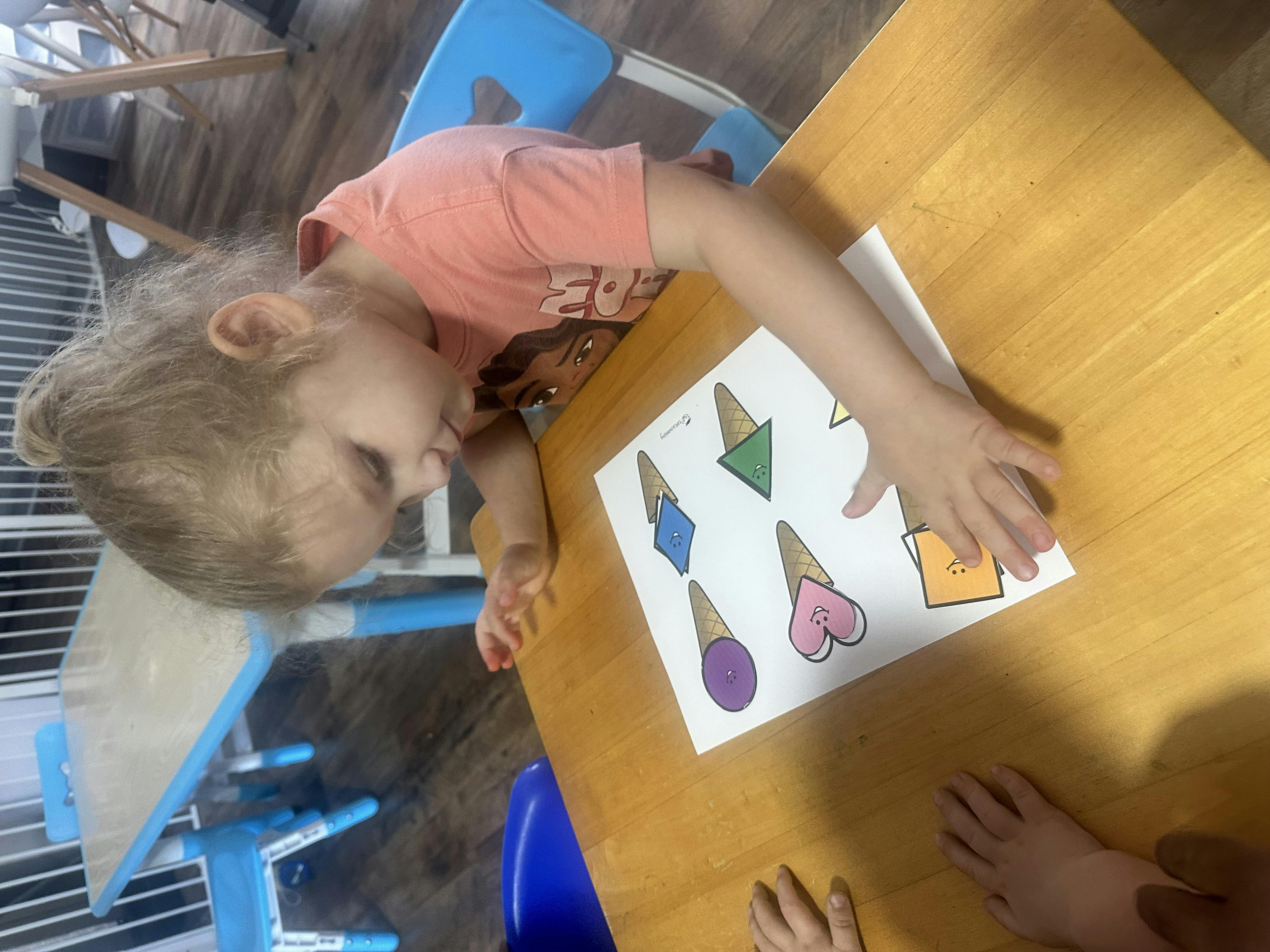 Child looking at a paper with colorful shapes on a table