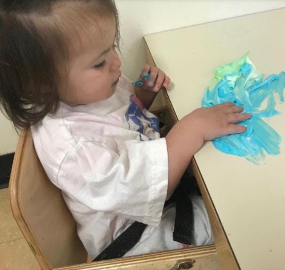 Child in high chair playing with blue and green paint on a table