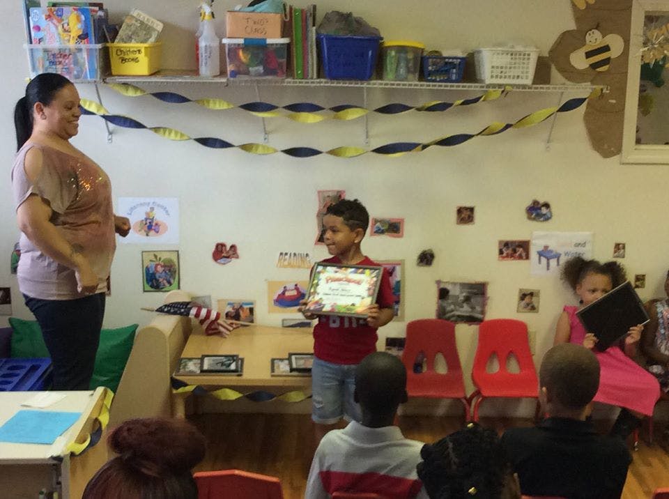 Adult and child standing, child holding a certificate in a classroom