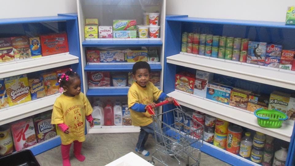 Two children in a play grocery store with shelves of food items