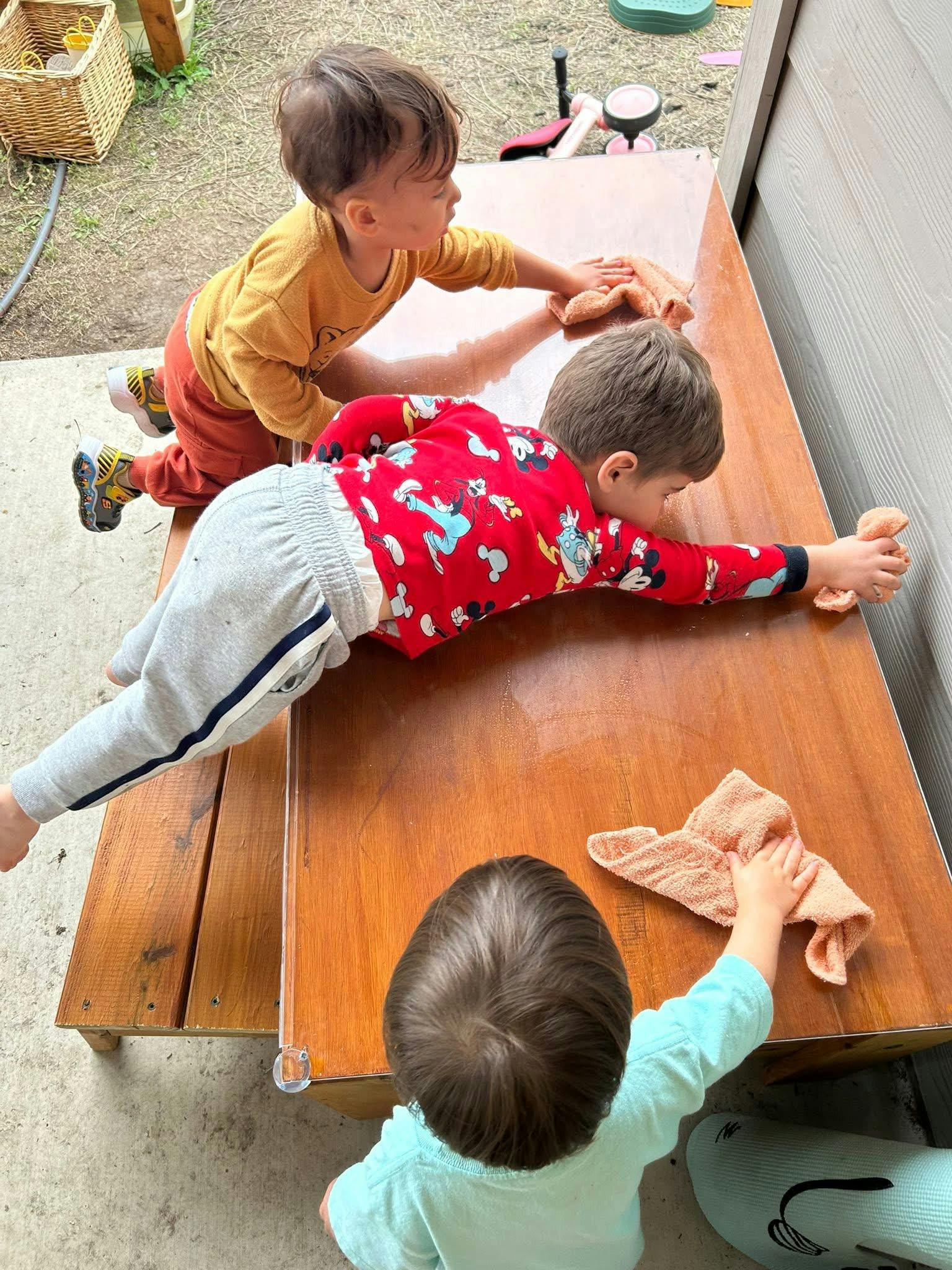 Three children cleaning a wooden table with cloths