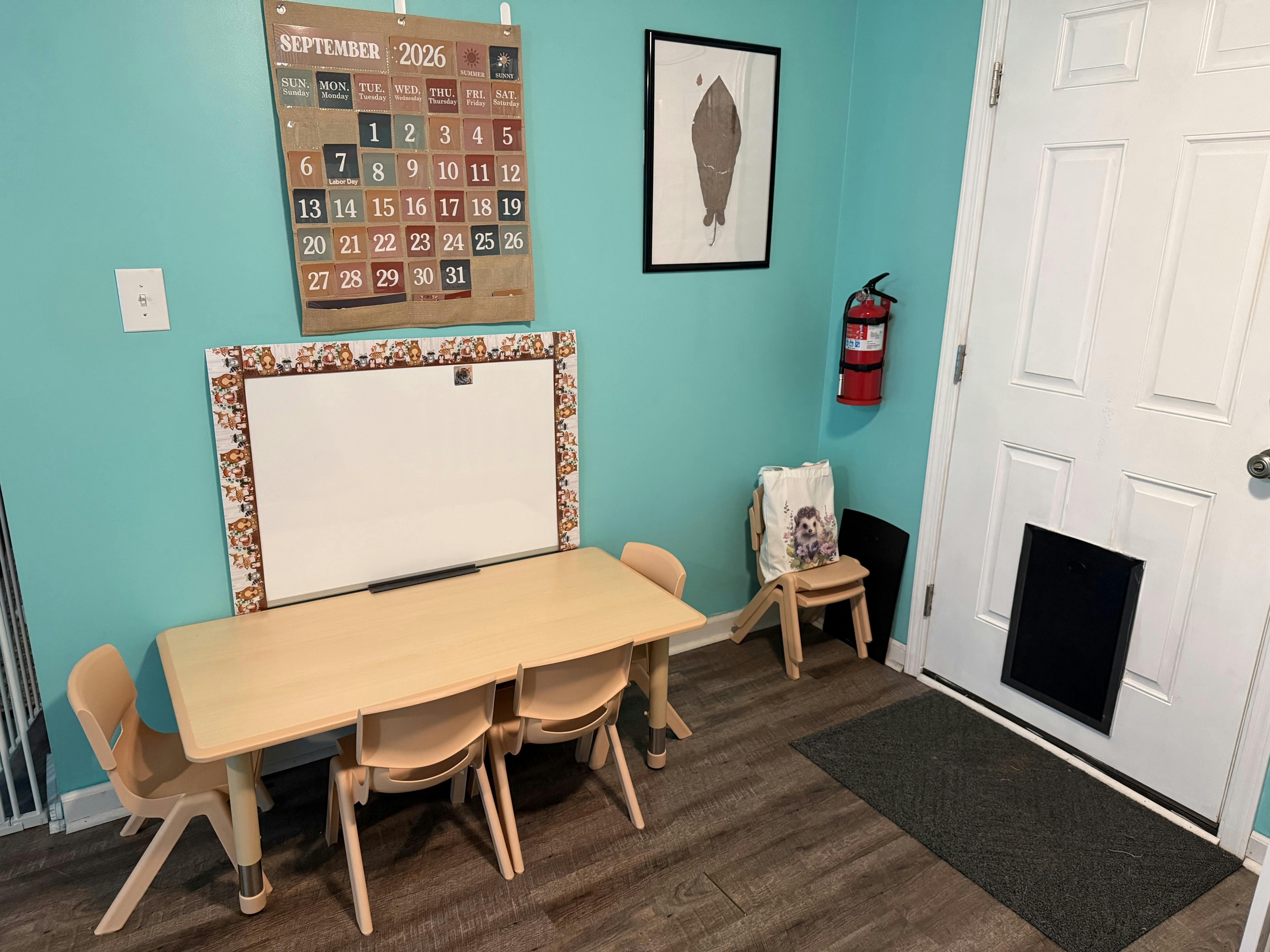 Child-sized table and chairs with a whiteboard and calendar on a teal wall