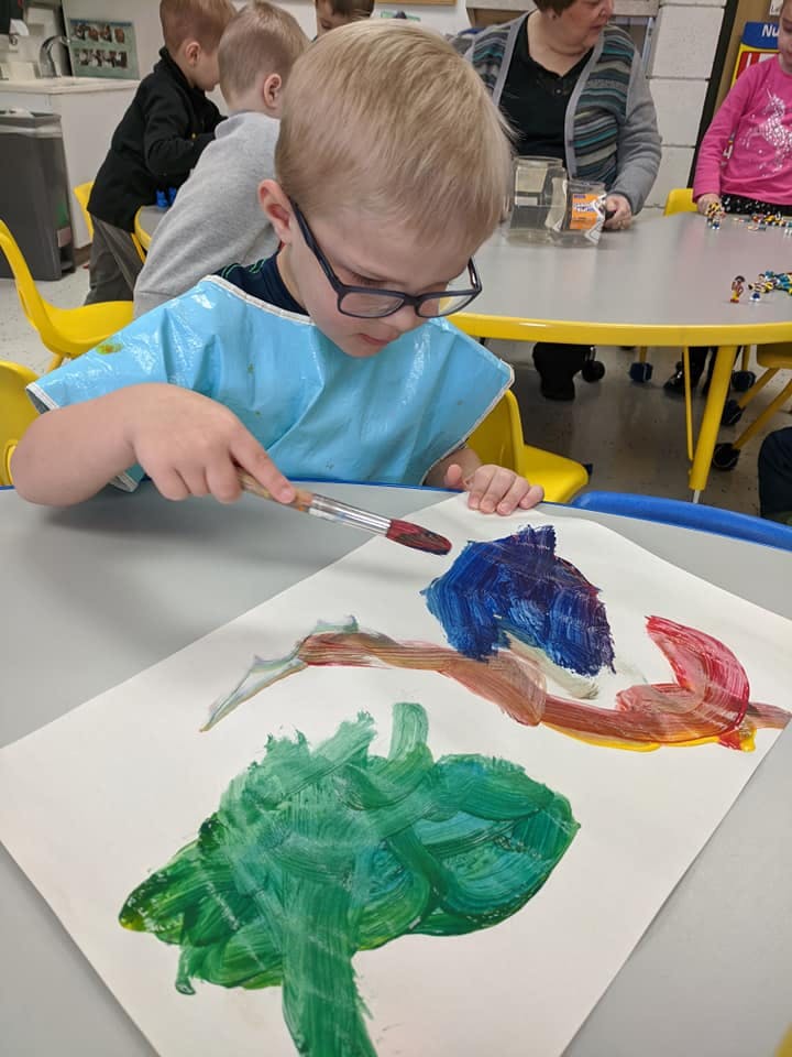 Child in glasses and smock painting on paper with a brush